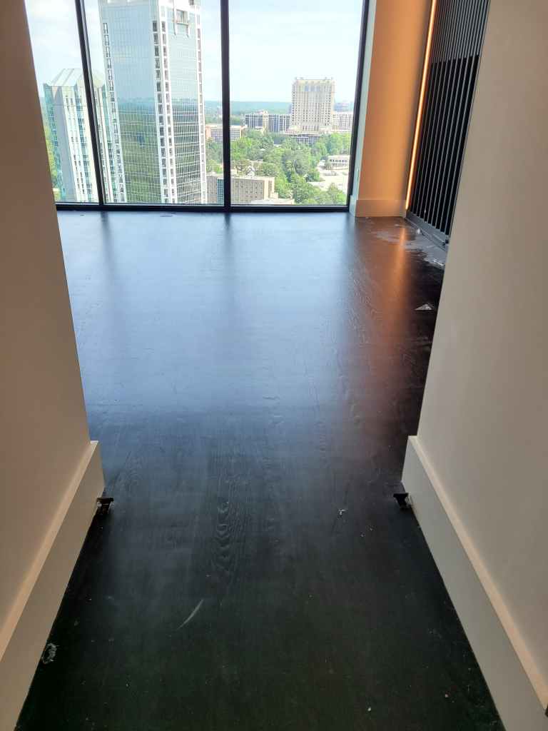 Existing dark-stained engineered hardwood in a Buckhead high-rise hallway before removal for white oak herringbone installation.