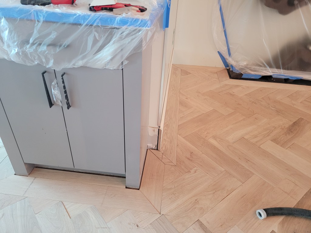 White oak 7-inch border running along the kitchen cabinetry base in a Buckhead high-rise, fitted to the herringbone field.
