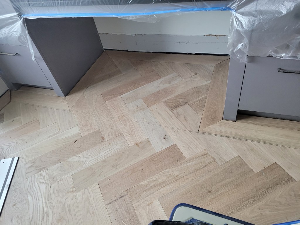 White oak tongue-and-groove border meeting the herringbone field in a Buckhead high-rise, mitered corner detail.