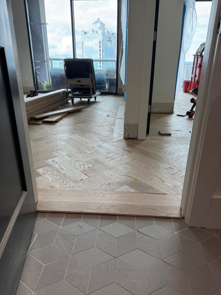 Custom white oak transition at a bathroom threshold in a Buckhead high-rise, small boards arranged in varying grain directions.