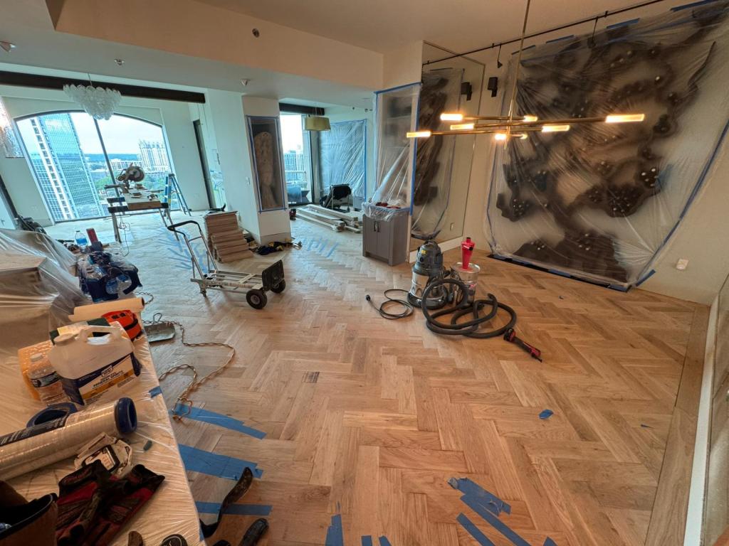 Dust-contained sanding of the white oak herringbone floor in a Buckhead high-rise, with artwork wrapped and protected nearby.