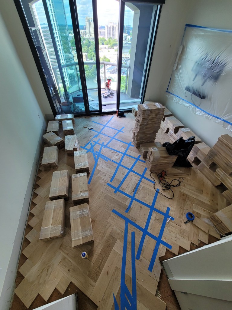 White oak herringbone installation in progress in a Buckhead high-rise, boards set with staged material along the window wall.
