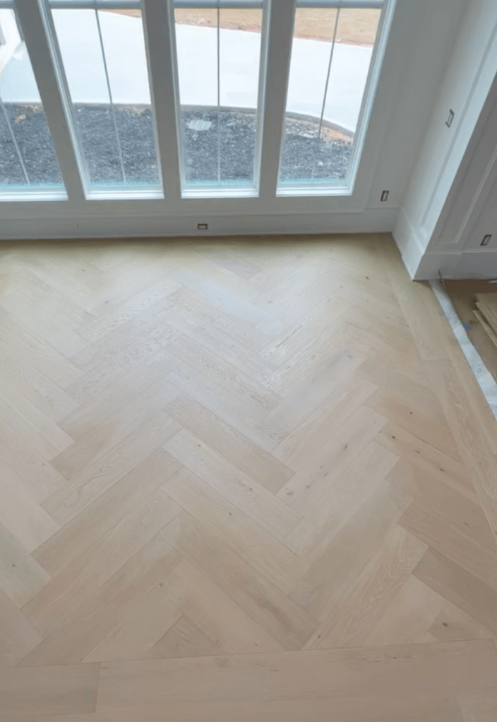 Custom herringbone installation with tongue-and-groove border using prefinished engineered oak flooring in an Atlanta dining room, adapted from straight-layout material with bevel-edge detail