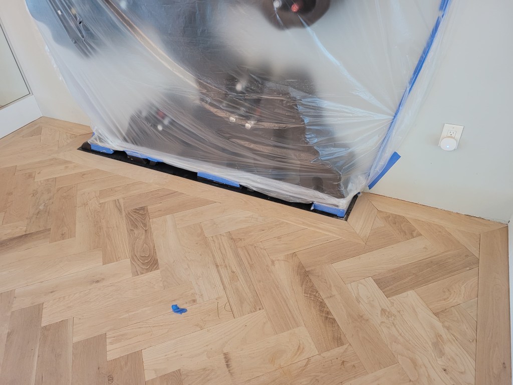 Large artwork wrapped in protective plastic with the white oak herringbone and 7-inch border fitted around its base, Buckhead high-rise.