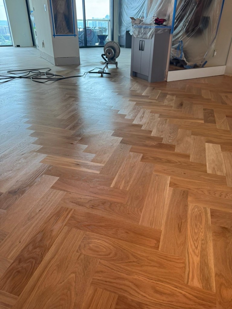 White oak herringbone floor during dust-contained sanding in a Buckhead high-rise.