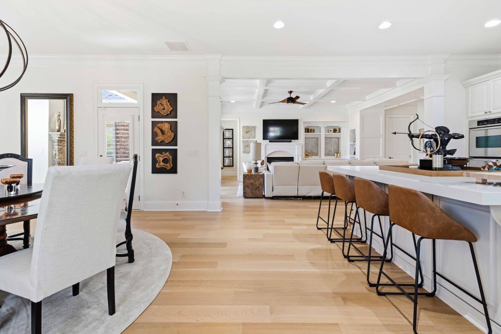 Rift and quartersawn white oak, site-finished with Bona Traffic HD, installed by Classy Flooring ATL in a Chateau Elan residence, Braselton GA — sightline from the dining area past the kitchen island seating into the great room.
