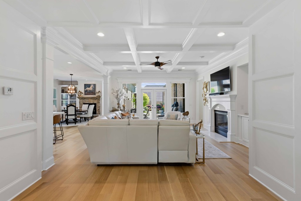 Rift and quartersawn white oak, site-finished with Bona Traffic HD, installed by Classy Flooring ATL in a Chateau Elan residence, Braselton GA — great room with coffered ceiling, fireplace, and open sightline to the kitchen and rear doors.