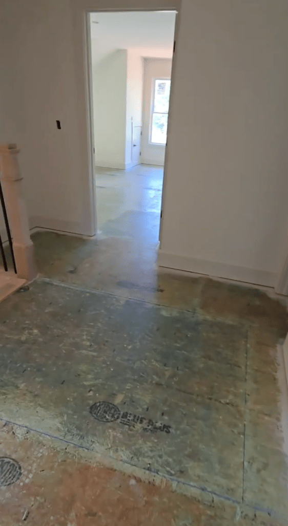 Plywood subfloor in Canton, GA new-construction home after Wakol PU 280 primer application, viewed through interior doorway with stair newel post at left