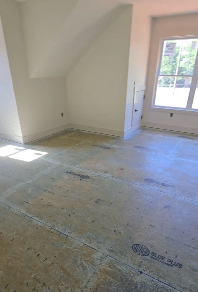 Upper-level bedroom plywood subfloor in Canton, GA new-construction home after Wakol PU 280 primer application, window on right and dormer ceiling at left