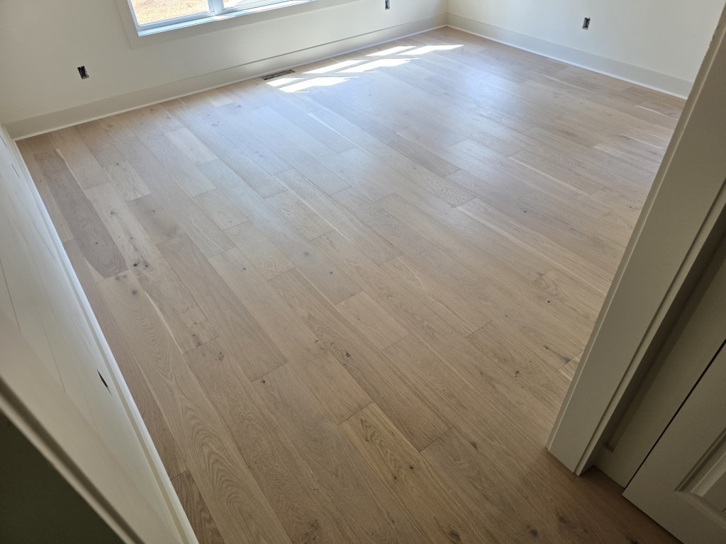Finished RW Floors Kells European white oak flooring in a bedroom in Canton, GA, showing 7-1/2″ wire-brushed planks running across the room with natural light from a window on the left