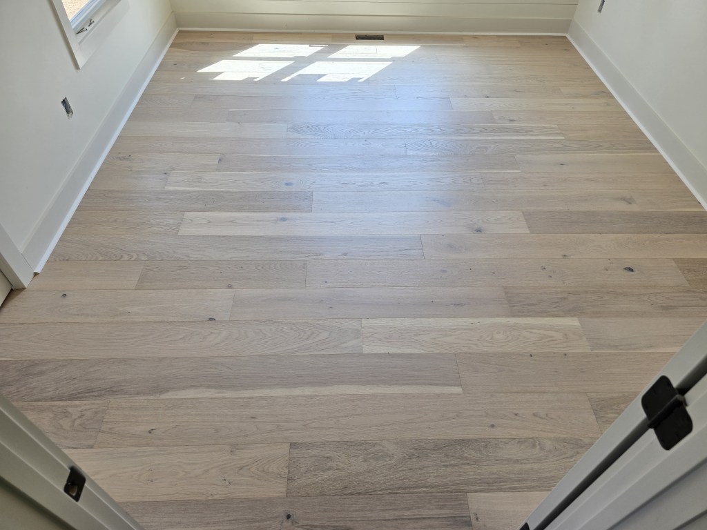 Finished RW Floors Kells European white oak flooring in a bedroom in Canton, GA, viewed from the doorway with sunlight falling across 7-1/2″ wire-brushed planks and a window on the far wall