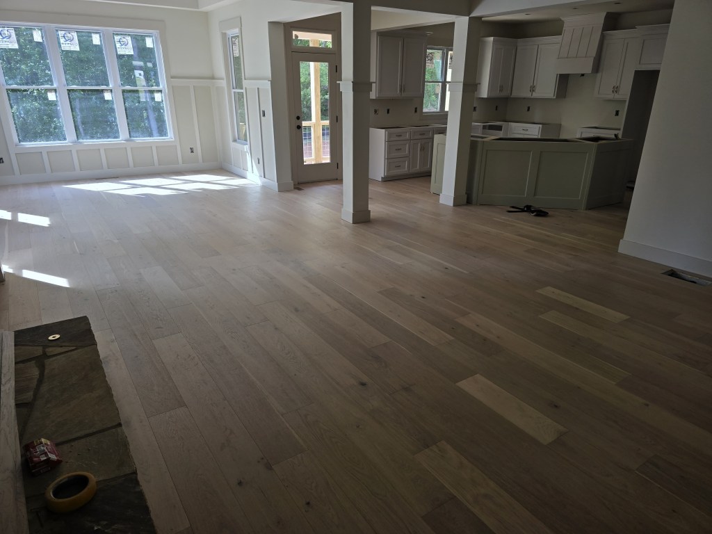 Finished RW Floors Kells European white oak flooring across the main level of a Canton, GA home, showing the living area with a wall of windows on the left and the kitchen with sage green island on the right