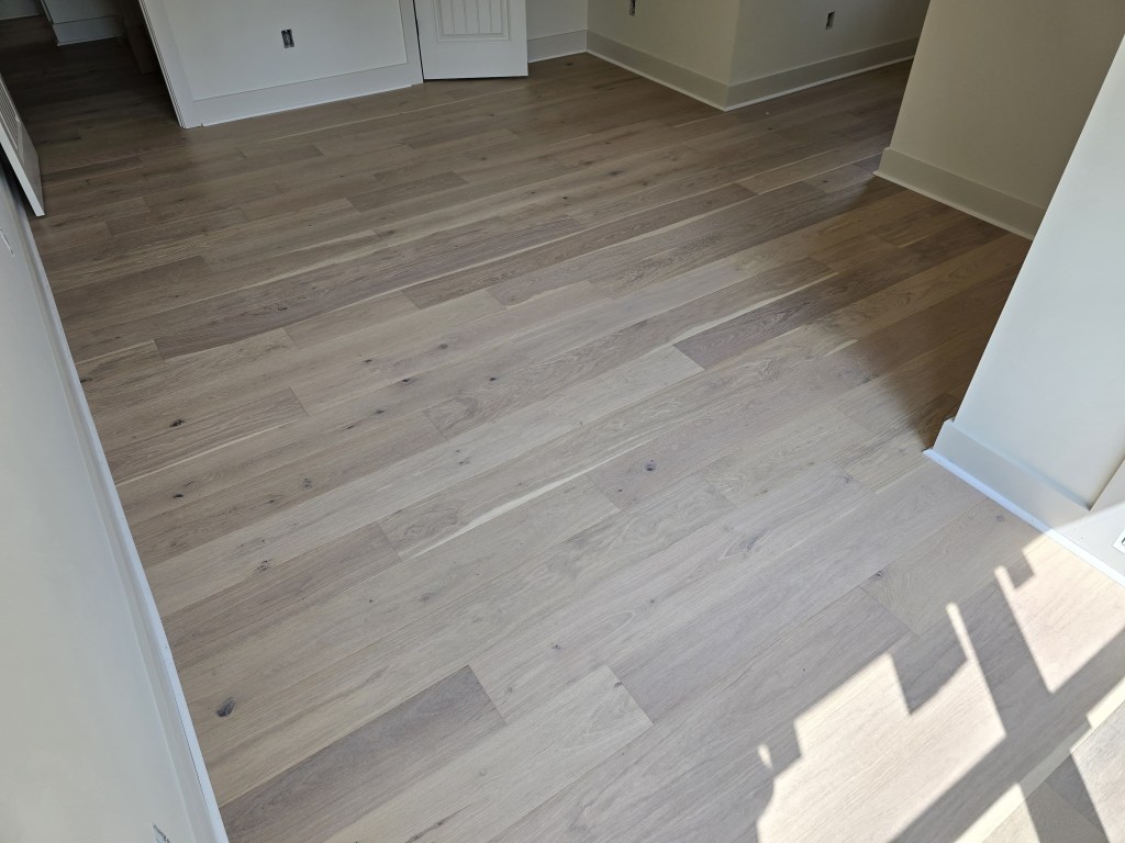 Finished RW Floors Kells European white oak flooring covering the full floor of a bedroom in Canton, GA, with sunlight falling across the wire-brushed planks near a doorway