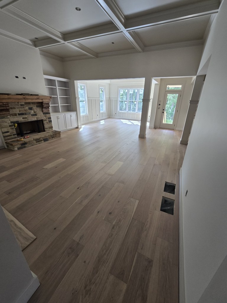 Finished RW Floors Kells European white oak flooring in a great room in Canton, GA, with a coffered ceiling, stone fireplace flanked by white built-ins, and a wall of windows at the far end