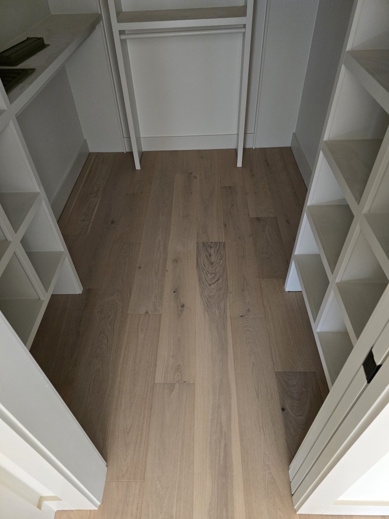 Finished RW Floors Kells European white oak flooring running through a walk-in closet in Canton, GA, with built-in white shelving and a vanity on either side