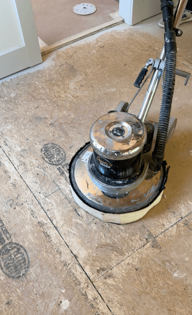 Rotary floor buffer on bare plywood subfloor during Canton, GA subfloor preparation, used to spot-sand high points and remove dried drywall compound