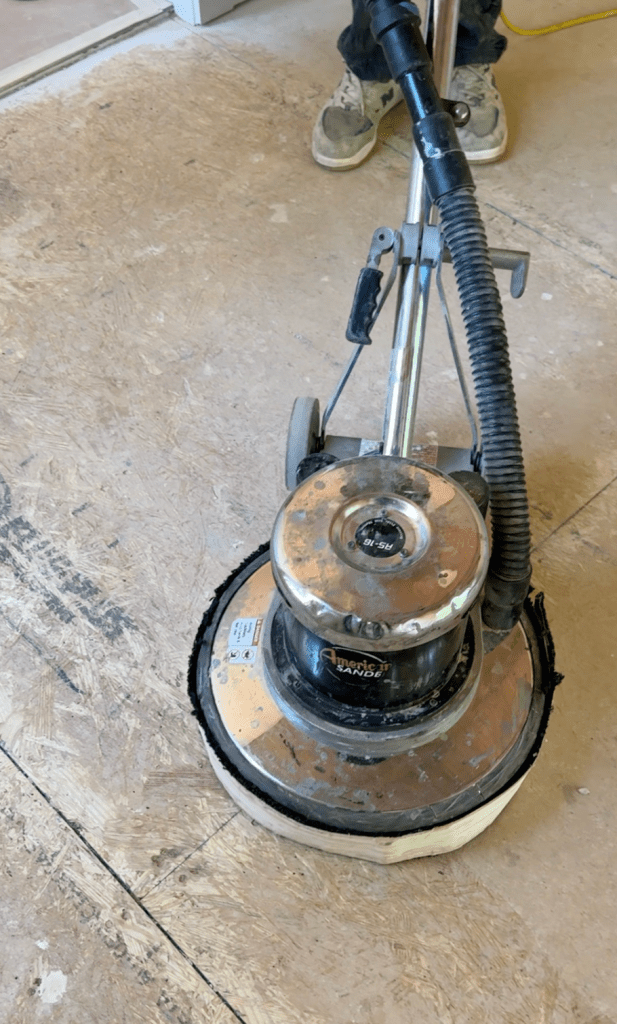 Rotary floor buffer being operated on bare plywood subfloor in a Canton, GA home during spot-sanding of high points and removal of dried drywall compound