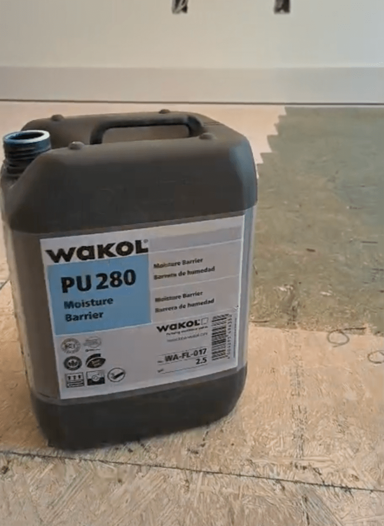 Wakol PU 280 Moisture Barrier substrate primer container on the plywood subfloor in a Canton, GA home, with primed and unprimed plywood visible behind it