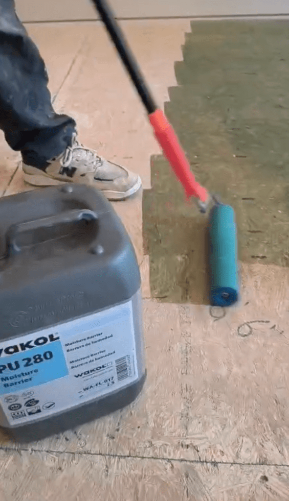 Wakol PU 280 substrate primer container next to the Loba micro-fiber roller on the plywood subfloor in a Canton, GA home, with the primed area visible alongside unprimed plywood