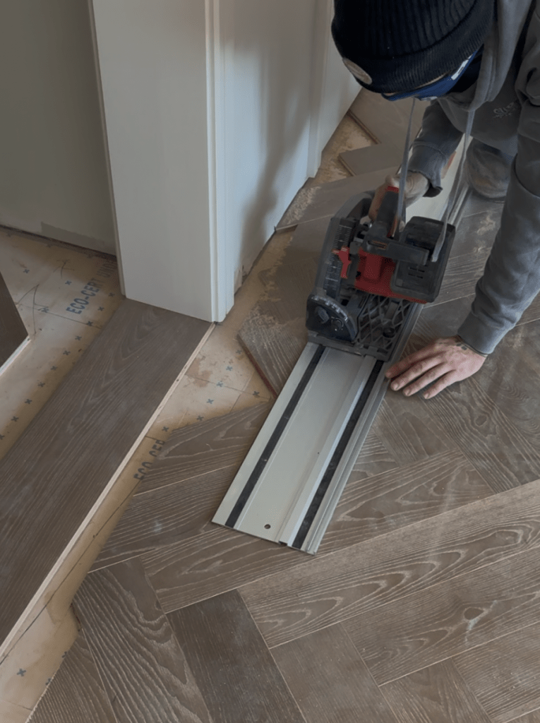 Classy Flooring ATL installer making a track-saw cut along the herringbone field on its guide rail