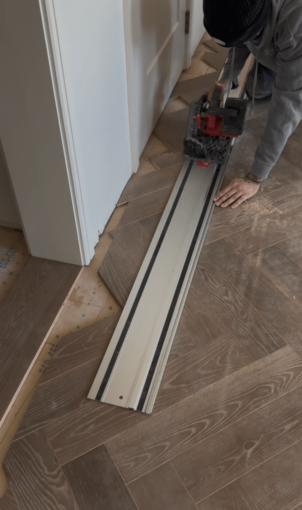 Classy Flooring ATL installer running a track saw down the guide rail to cut the herringbone border line