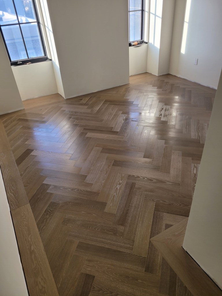 Finished herringbone field meeting the custom border and a straight-lay threshold in European Ash