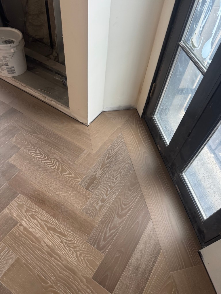 European Ash herringbone field meeting the custom border at a glass door threshold and wall corner
