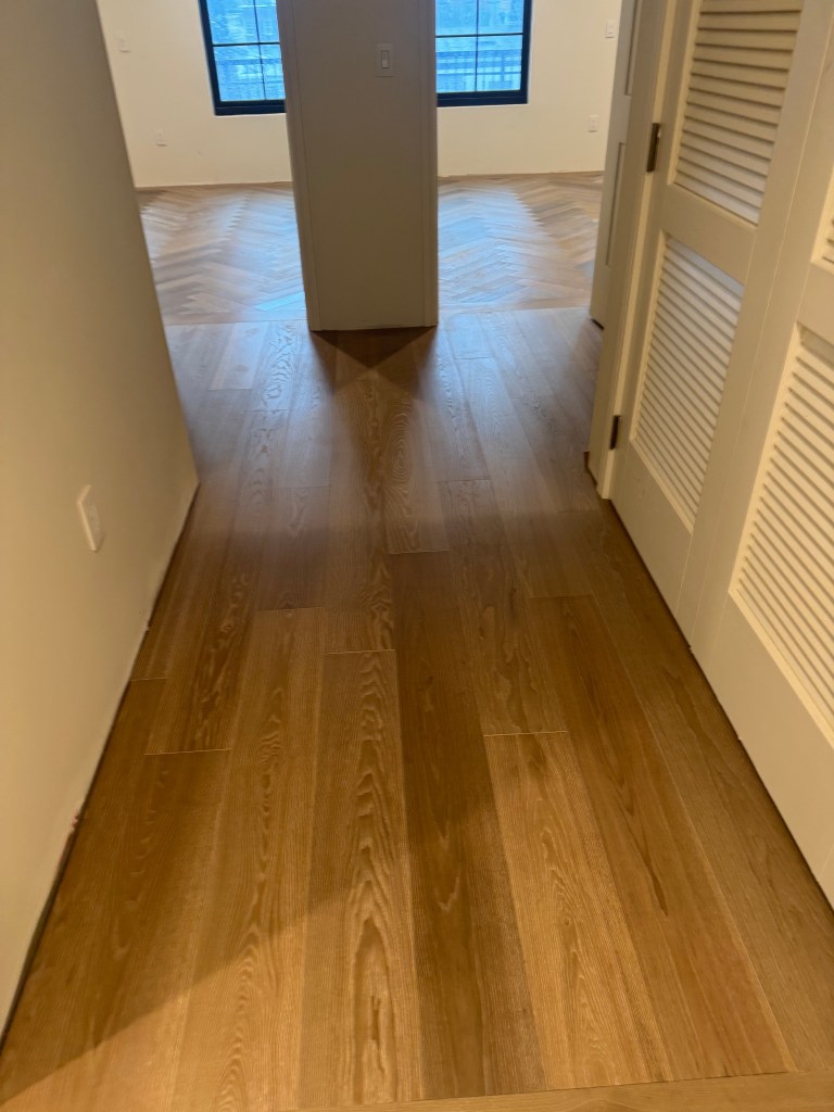 Straight-lay European Ash hallway with louvered closet doors in a Savannah penthouse, herringbone room beyond