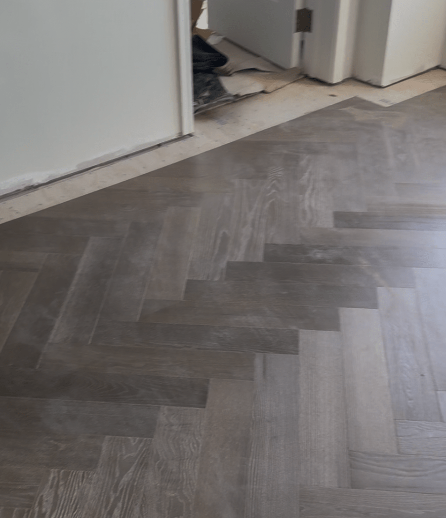 Laid herringbone field meeting the open border perimeter near a doorway, work continuing in the room beyond