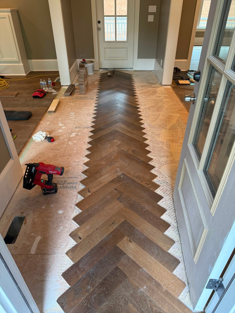 Fabricated engineered herringbone field being installed along a Dunwoody, GA entrance hallway over a troweled adhesive bed on plywood