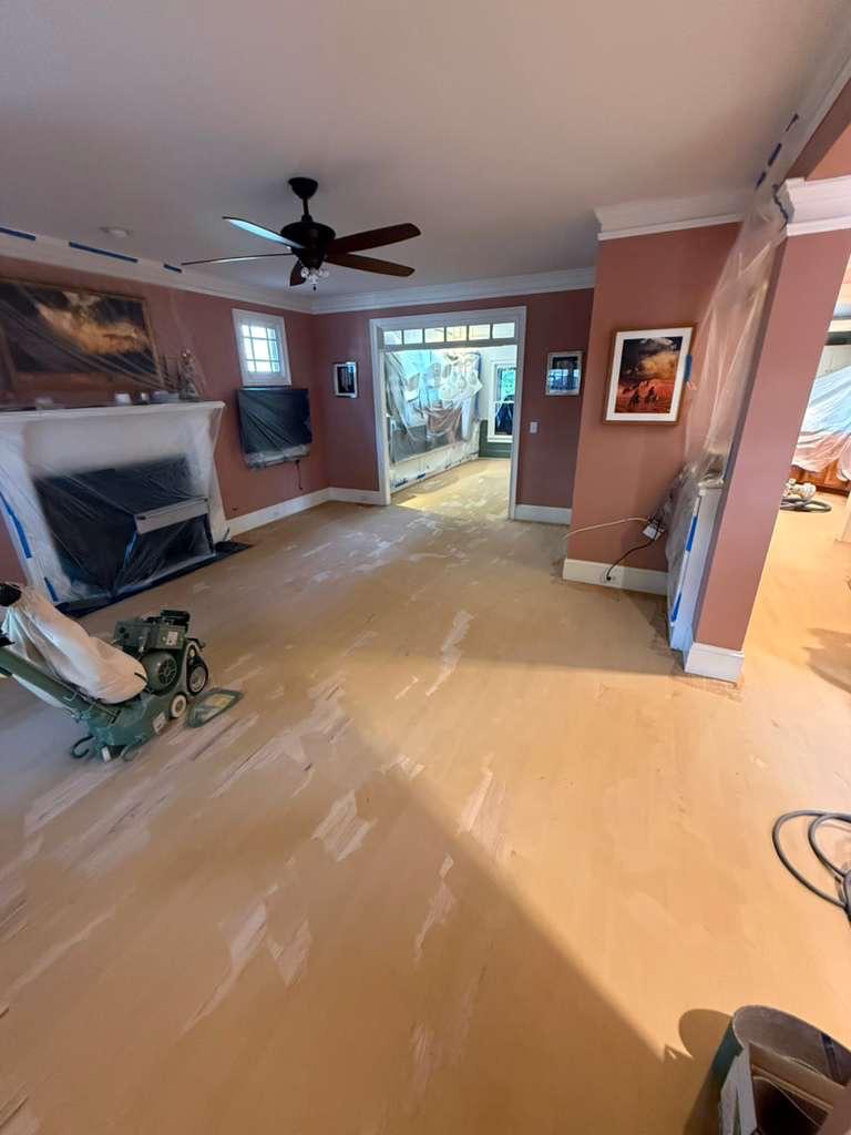 Red oak floor with trowel-applied wood filler during refinishing in Atlanta, fireplace and furnishings covered in plastic dust containment