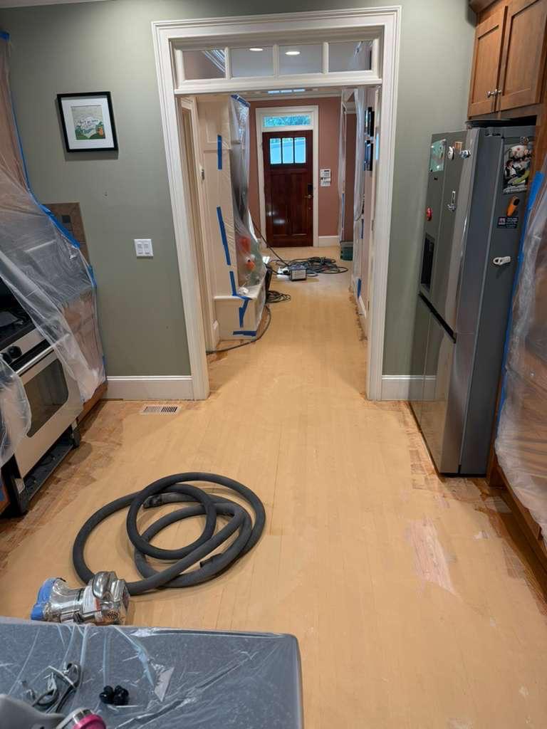 Kitchen and hallway red oak floor with wood filler applied, dust extraction hose on the floor and appliances sealed in plastic during dustless refinishing in Atlanta