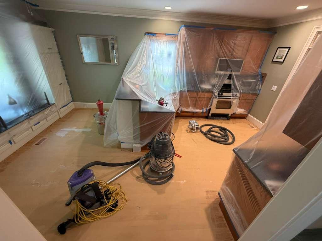 Dust extraction vacuum on a red oak floor with wood filler applied, kitchen cabinetry and appliances fully tented in plastic during dustless refinishing in Atlanta