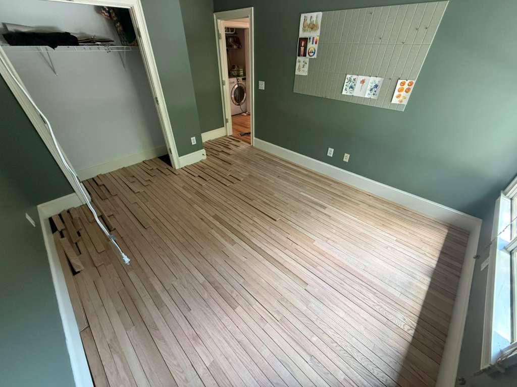 Unfinished red oak boards racked and partially installed in a former carpeted bedroom during a flooring project in Atlanta, end joints staggered across the room
