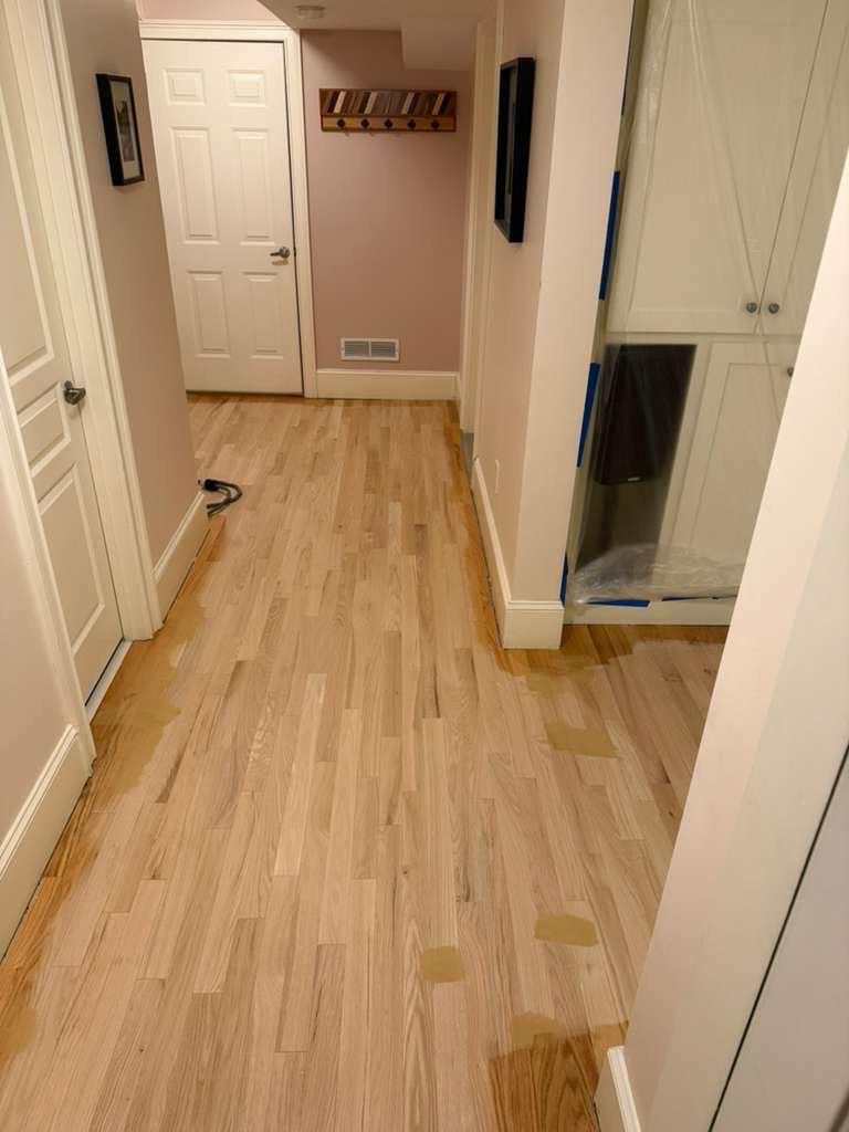 Red oak hallway floor sanded to bare wood during refinishing in Atlanta, wood filler visible in patches at board gaps, closet contents covered in plastic