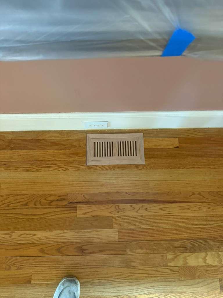 New unfinished flush-mount vent installed in an old red oak floor before sanding during a refinishing project in Atlanta, raw vent contrasting with the worn amber finish
