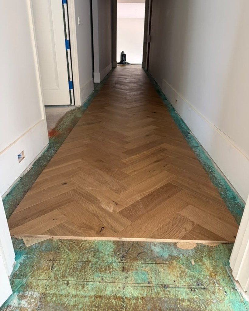 European white oak herringbone laid down a hallway with the perimeter left open for the custom border and brass inlay, before those were installed