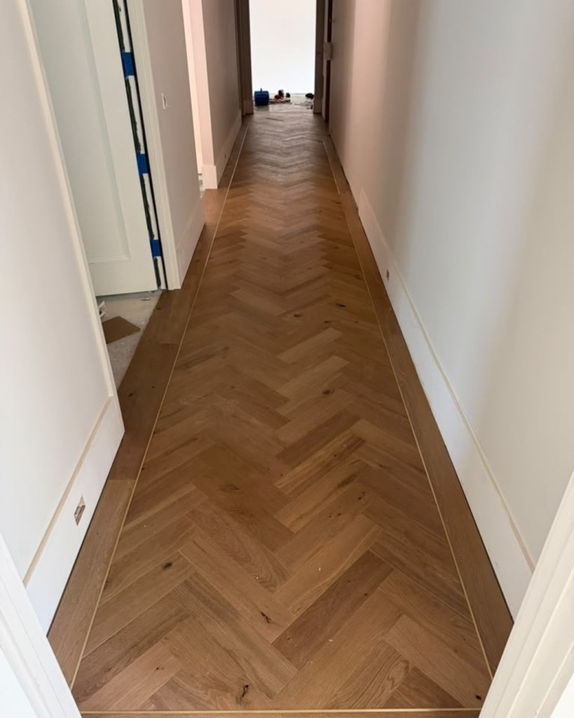 Finished European white oak herringbone hallway framed by a custom border with a brass feature strip running the perimeter and through the threshold