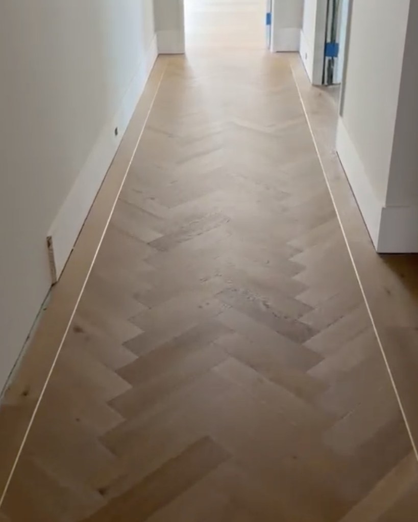 Finished European white oak herringbone running down a hallway, framed by a custom border with a brass feature strip tracing the border line on both sides