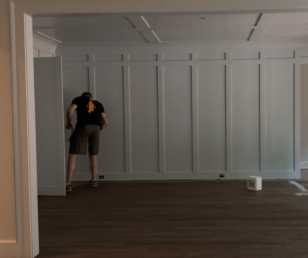 Classy Flooring ATL installer working at a doorway on a dark hardwood floor during a refinishing project in a Buckhead, Atlanta room with a paneled accent wall.