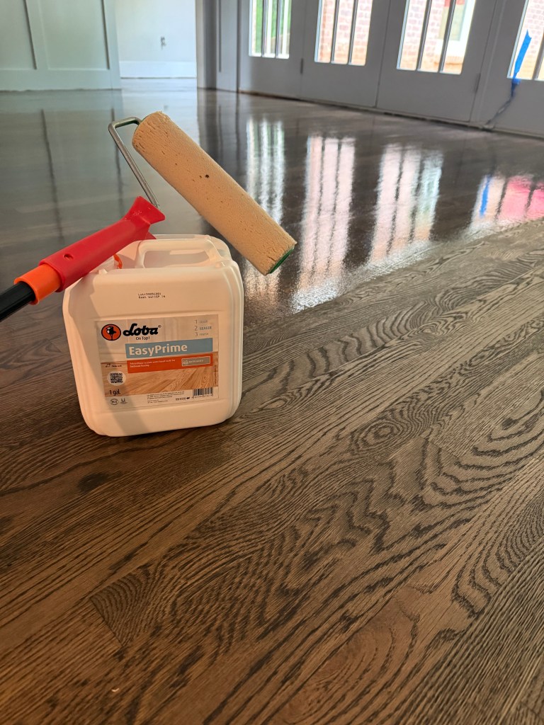 LOBA EasyPrime sealer and a roller resting on a Jacobean-stained white oak floor during a refinishing project in a Buckhead, Atlanta residence by Classy Flooring ATL.