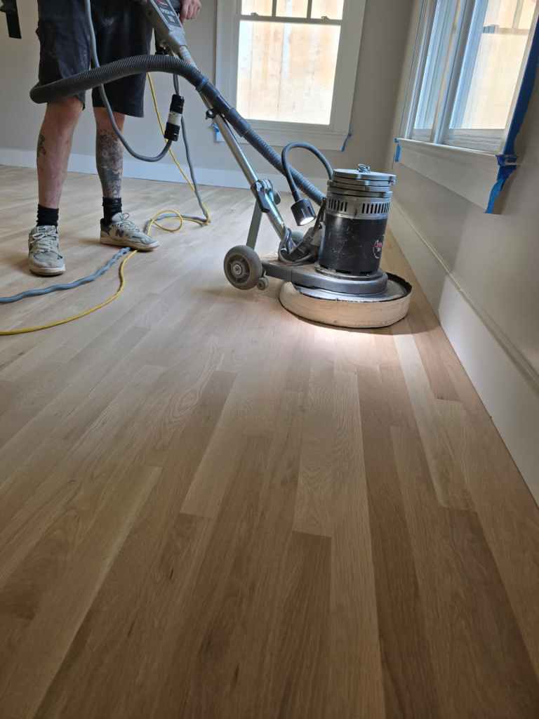 Close view of an FG Discus planetary sander refining a bare hardwood floor during a refinishing project in a Buckhead, Atlanta residence by Classy Flooring ATL.