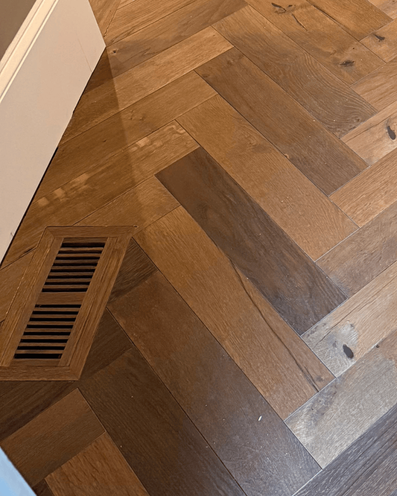 Flush-mount white oak vent set into the fabricated engineered herringbone floor, color-matched so it sits level with the surface, Dunwoody, GA