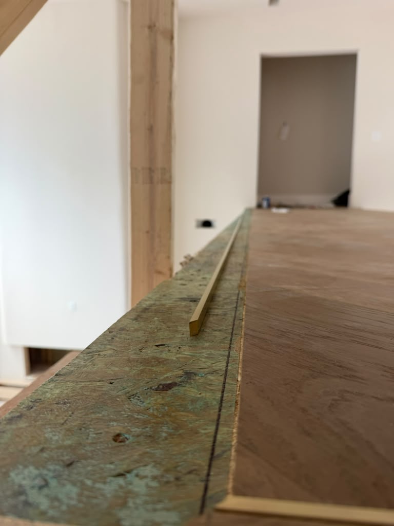 Close-up of the cut perimeter of the European white oak herringbone field on the catwalk, with solid brass bar stock staged before the brass inlay and custom border installation in Woodstock, Georgia.