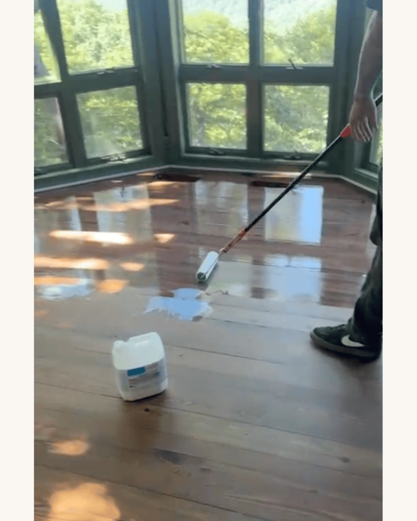 Rolling AquaSeal CeramicStar finish onto the restored reclaimed heart pine floor with the container of finish on the floor, Big Canoe, Georgia