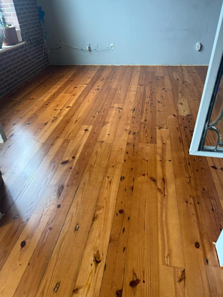 Refinished heart pine flooring in a warm amber tone against a pale grey-blue wall and open doorway, Roswell, Georgia