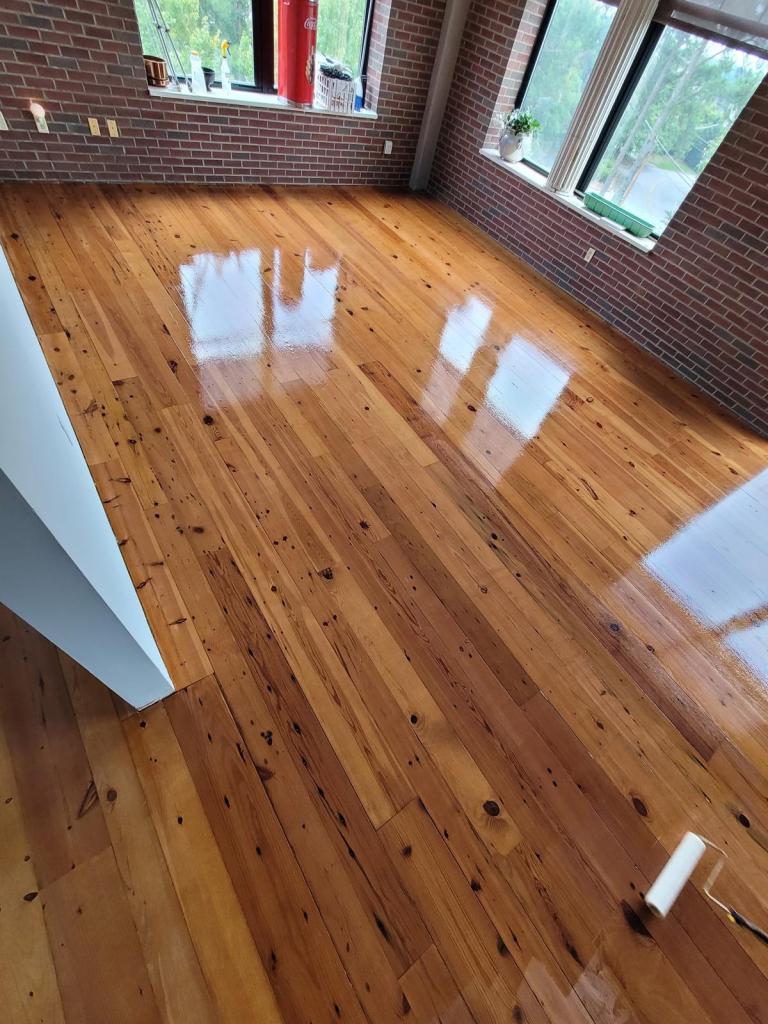 Waterborne finish being rolled across a stained heart pine floor, wet coat visible against the drier area, Roswell, Georgia