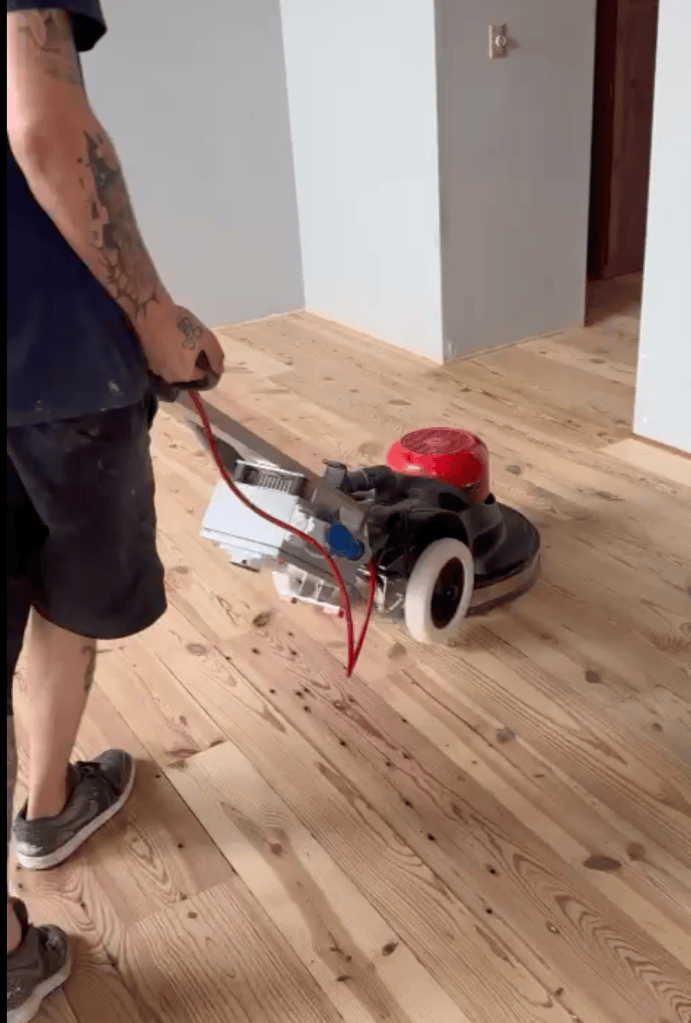 Classy Flooring ATL crew member running a hose-connected planetary sander across a sanded heart pine floor, Roswell, Georgia