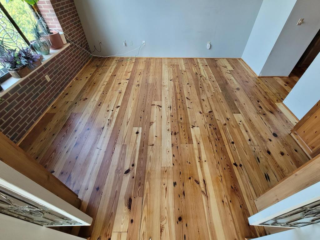 Heart pine flooring in a pale waterborne finish before refinishing, replacement boards reading lighter than the surrounding field, Roswell, Georgia