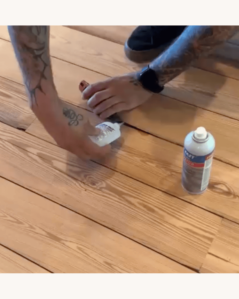 Classy Flooring ATL crew member working glue into a splinter repair in reclaimed heart pine flooring, Stick Fast spray activator can alongside, Big Canoe, Georgia
